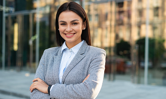 Woman in a gray blazer smiling confidently with arms crossed