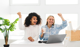 Two women celebrating at a desk with a laptop
