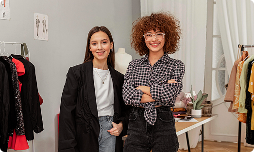 Two smiling women stand in a stylish clothing boutique