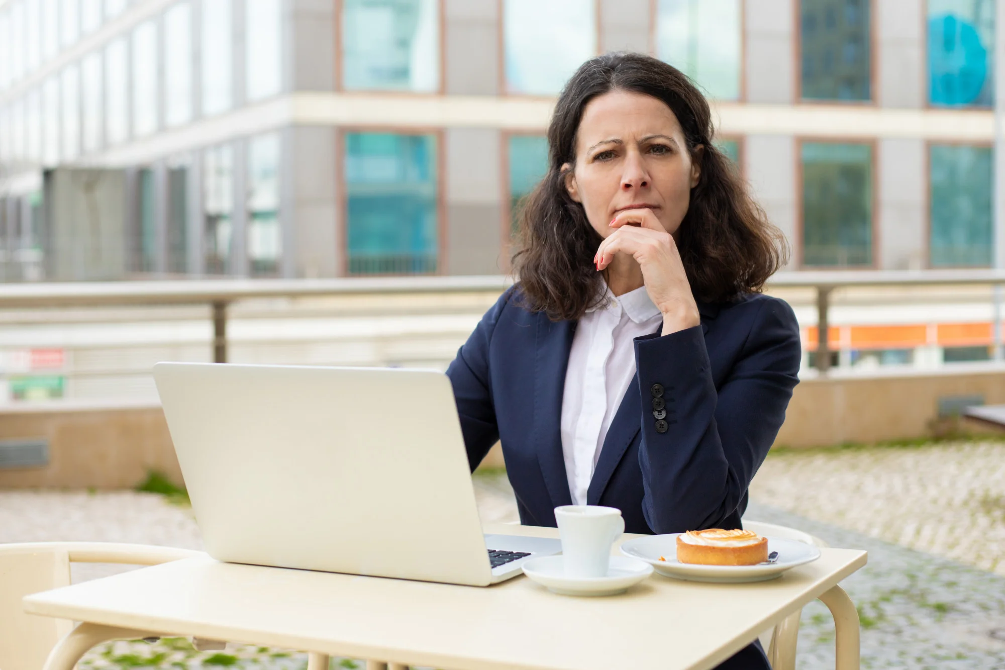 Woman in a navy blazer sits at an outdoor table with a laptop