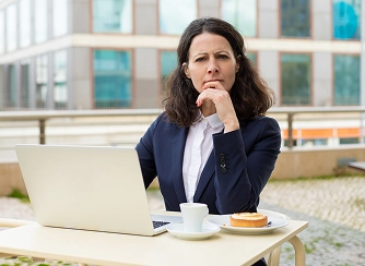 Woman in a navy blazer sits at an outdoor table with a laptop