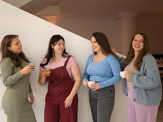 Four women stand together, smiling and chatting