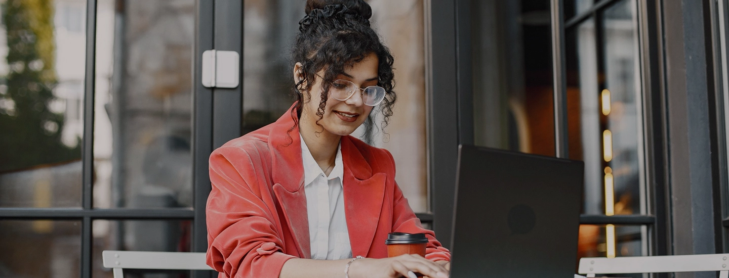 Woman in a red blazer and glasses works on a laptop