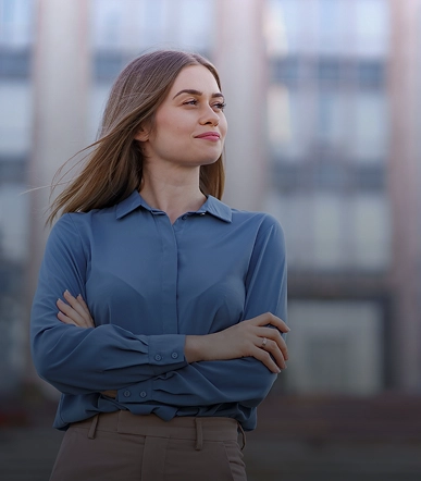 Woman stands outdoors, arms crossed, wearing a blue blouse