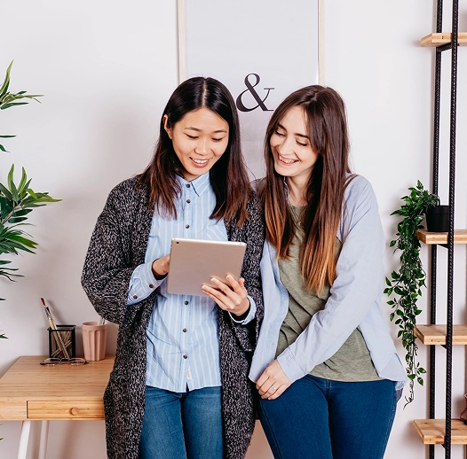 Two smiling women standing and looking at a tablet