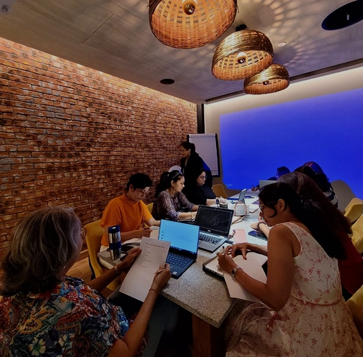 Group of people sit around a table in a conference room with laptops and papers