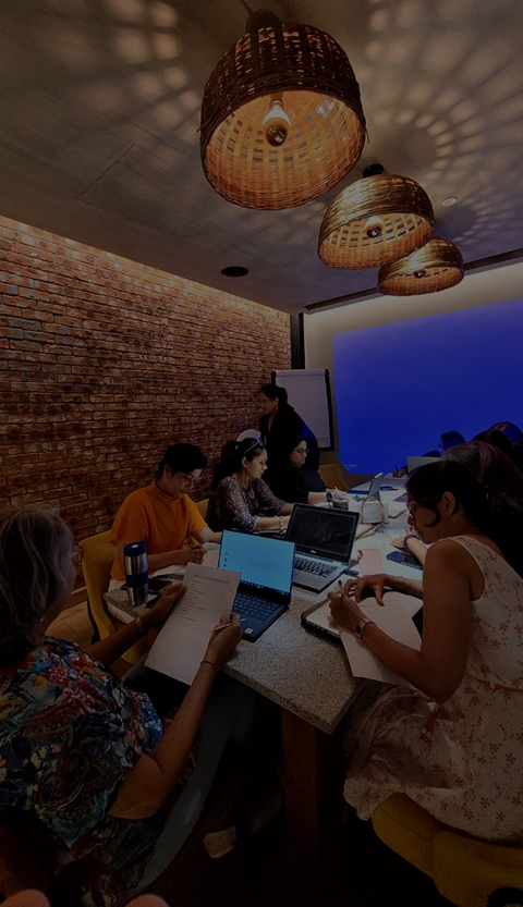Group of people sit around a table in a conference room with laptops and papers